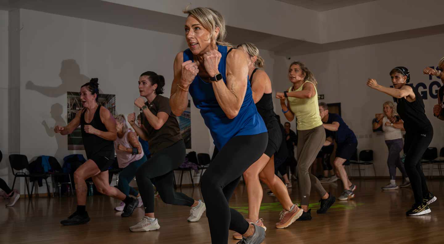 A group fitness class performing fast-paced punch and step movements in a studio with wooden flooring.