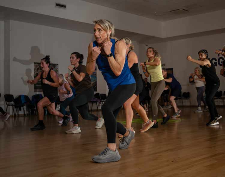 A group fitness class performing fast-paced punch and step movements in a studio with wooden flooring.