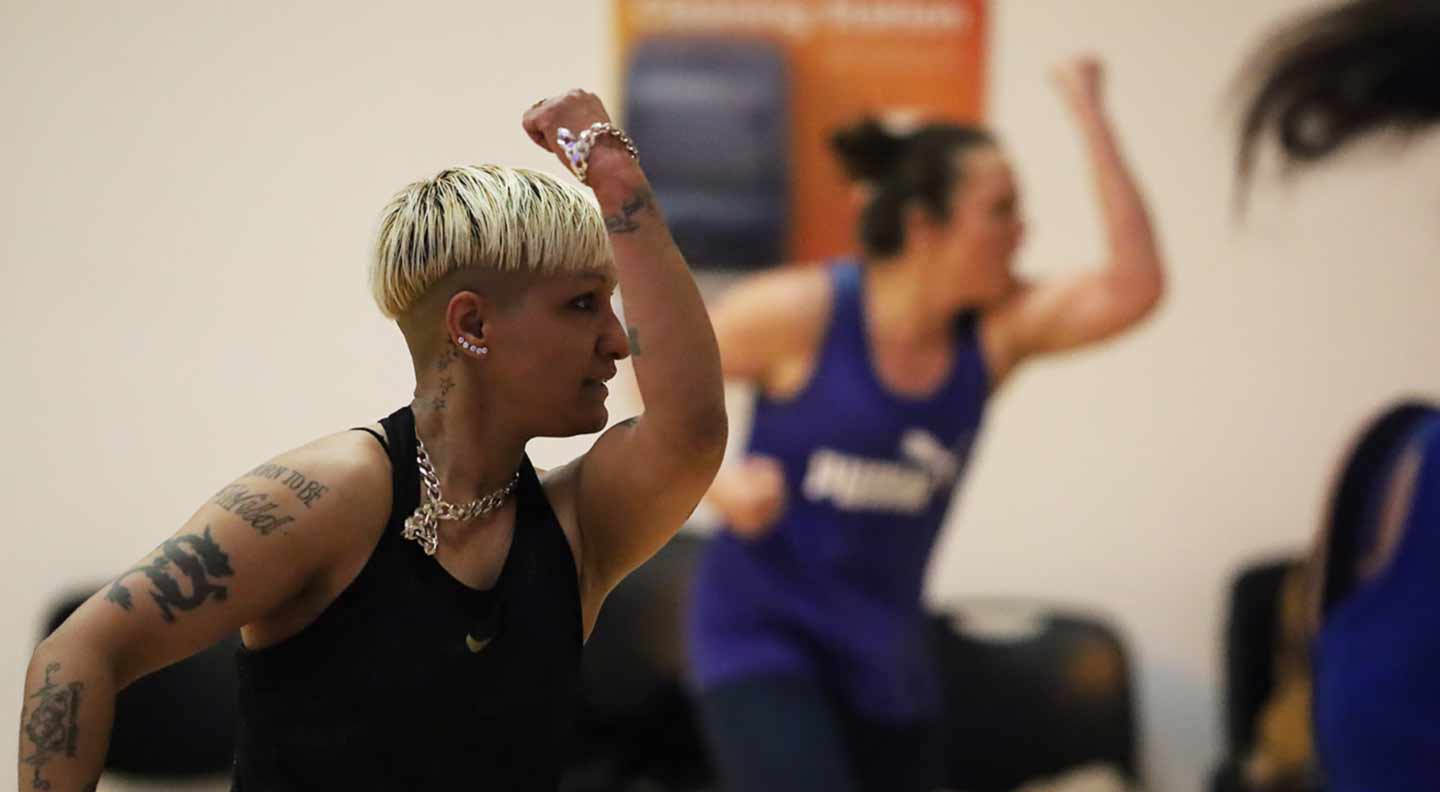 A group fitness class in motion, with a participant in the foreground raising an arm during an energetic routine.