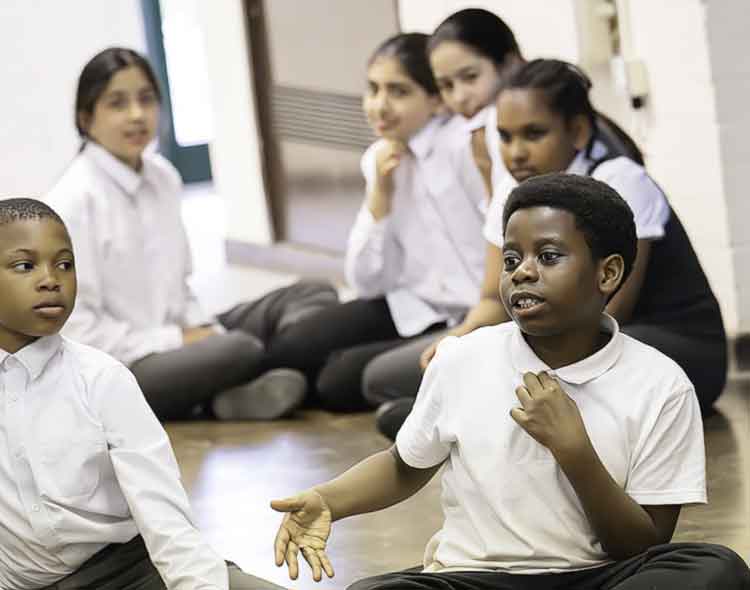 Group of children wearing school uniforms seated on floor in a classroom - attentively listening and smiling during a class workshop.
