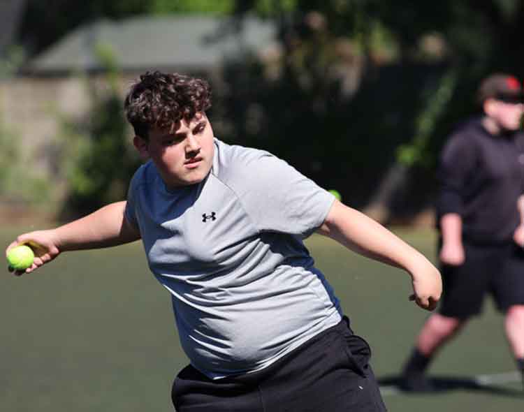 A boy throwing a ball during an outdoor sports activity on a field, with another participant in the background.