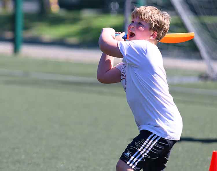 Young boy swinging a plastic bat during an outdoor sports activity on a playing field.