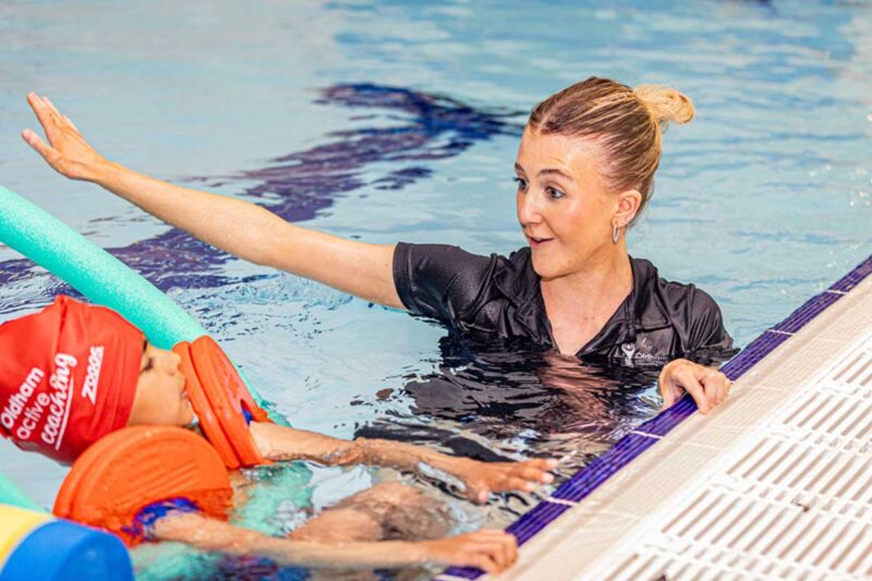Instructor in pool teach a group of children with floats how to swim and water safety