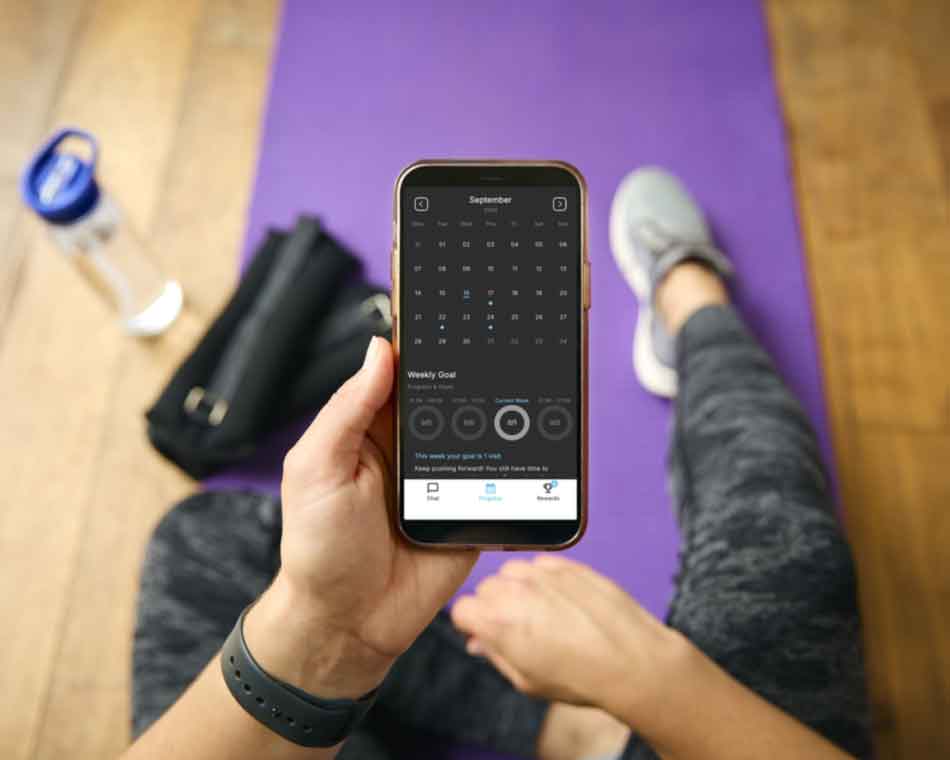 using the app on phone in gym during workout - screen showing work out calendar - matt on gym floor with water bottle